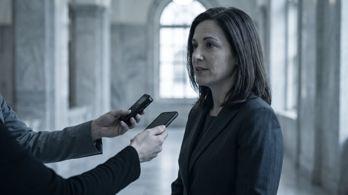 An executive answering questions in a courthouse corridor while a reporter holds out an audio recorder and a phone